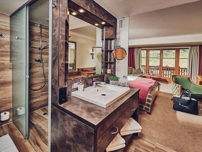 Moderní hotelový pokoj s dřevěnými detaily, postelí, sprchou a balkonem s výhledem.