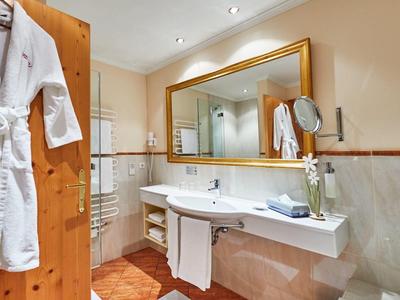 Světlá koupelna s velkým zrcadlem, bílým umyvadlem, ručníky a dřevěnými dveřmi s županem.