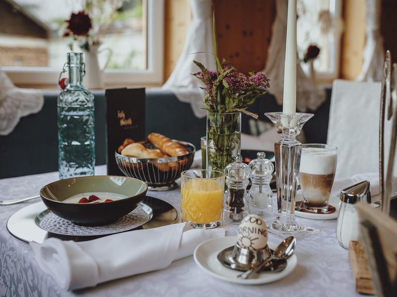 Elegantní snídaně s pomerančovým džusem, kávou, pečivem a květinami na bílém prostřeném stole.