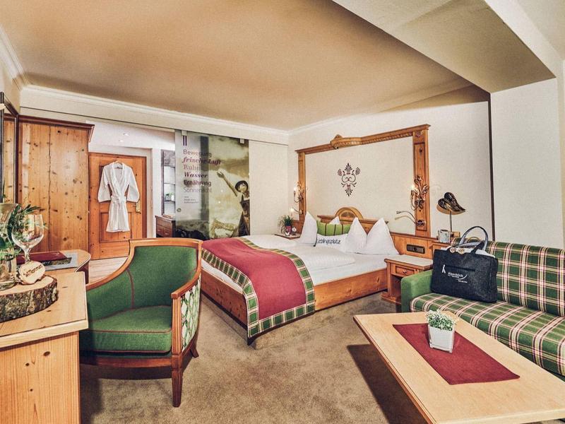 Příjemný hotelový pokoj s manželskou postelí, pohovkou, televizí a rustikálním dřevěným nábytkem.