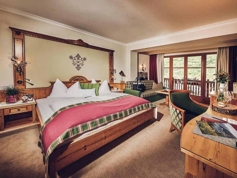 Pohodlný hotelový pokoj s dvojlůžkem, posezením a balkonem s výhledem do zeleně.