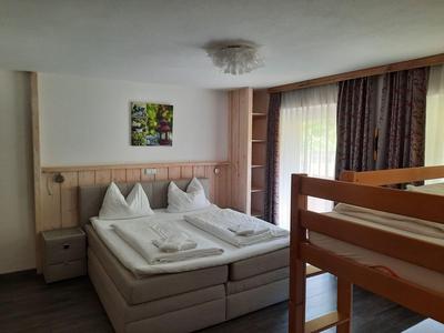 Chambre d'hôtel lumineuse avec lit double, lit superposé et rideaux à la fenêtre.