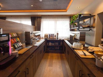 Modern hotel lounge with coffee machine, breakfast items, and natural light.