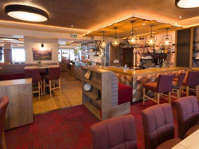 Bar d'hôtel confortable avec chaises rouges, comptoir en bois et lumière chaude.