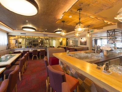 Bar d'hôtel accueillante avec comptoir en bois, chaises rouges et lumière chaude.