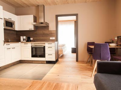 Cuisine d'hôtel moderne avec armoires blanches, sol en bois et vue sur une chambre.