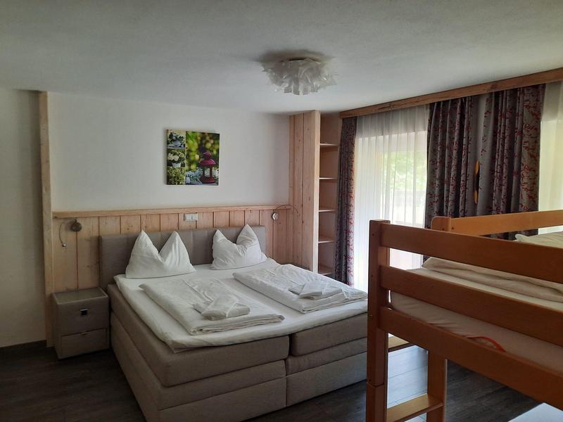 Cozy hotel room with double bed, bunk bed, nightstands, and curtains on a window.