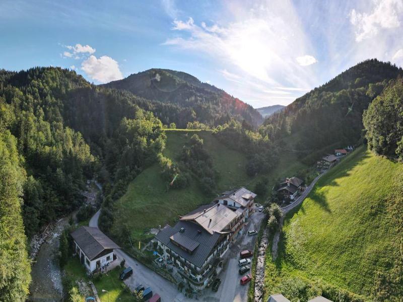 Hotel in a green valley surrounded by forested mountains under a blue sky.