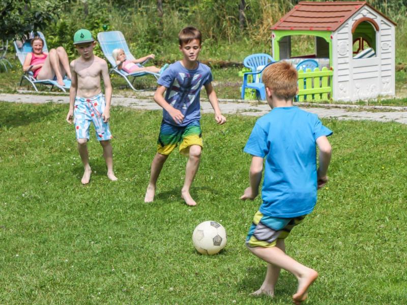 Children playing soccer on a lawn in front of a small playhouse in the garden.