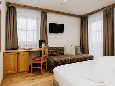 Pohodlný hotelový pokoj s postelí, pohovkou, televizí a malým psacím stolem.