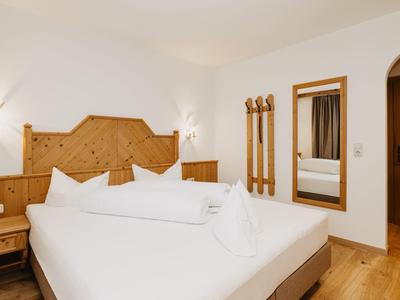 Světle zařízený hotelový pokoj s manželskou postelí, dřevěným nábytkem a velkým zrcadlem.