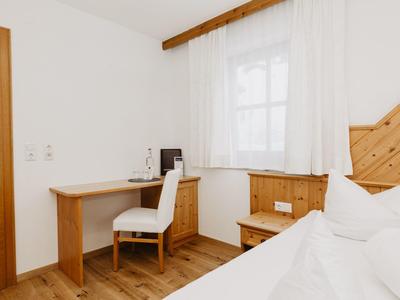 Světý hotelový pokoj s dřevěným nábytkem, psacím stolkem, židlí a pohodlnou postelí.