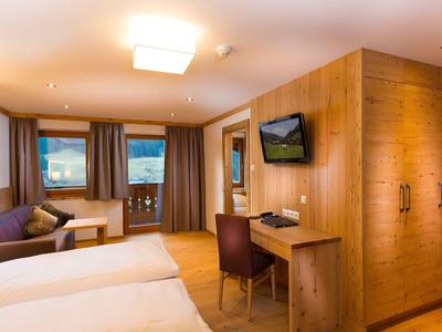 Pohodlný hotelový pokoj s manželskou postelí, dřevěným nábytkem a výhledem na hory oknem.