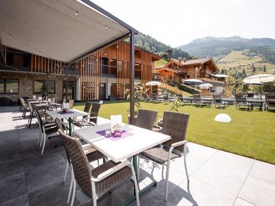 Moderner Außenbereich eines Hotels mit Tischen, Stühlen und Blick auf eine grüne Wiese und Berge.