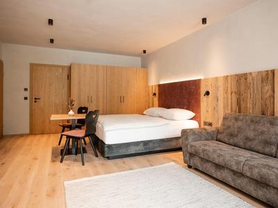 Moderní hotelový pokoj s velkou postelí, dřevěným obkladem a pohodlnou pohovkou.