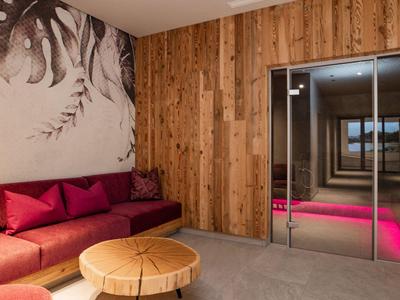 Moderní hotelová lounge s dřevěným obložením, červenou pohovkou a kulatým dřevěným stolem.