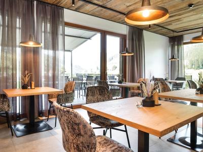 Moderní jídelní prostor s dřevěnými stoly a čalouněnými židlemi v hotelu s panoramatickými okny.