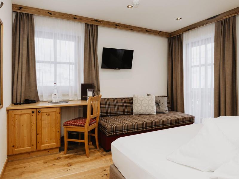 Pohodlný hotelový pokoj s postelí, pohovkou, televizí a malým psacím stolem.