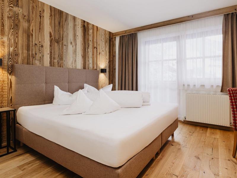 Pohodlná manželská postel s bílým povlečením v moderním hotelovém pokoji s dřevěnou zdí.