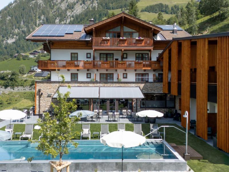 Hotel s venkovním bazénem, slunečníky a lehátky na pozadí hor.