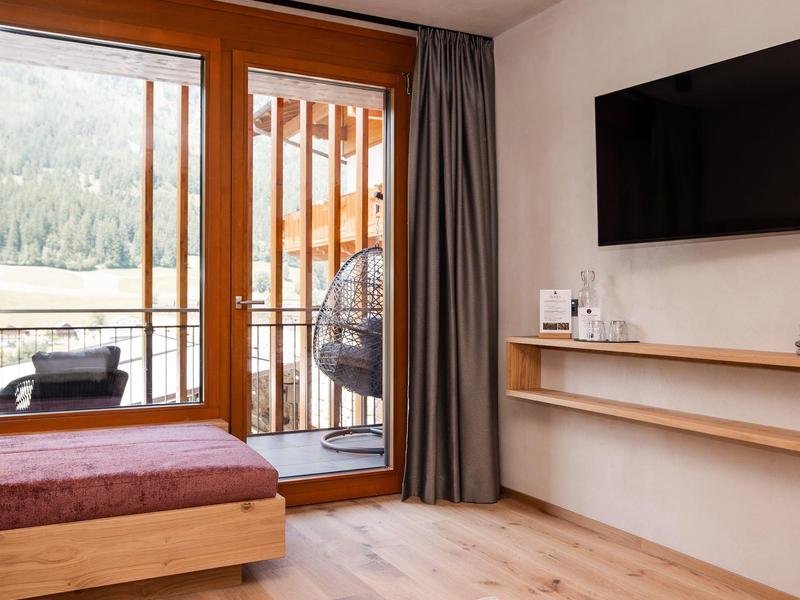 Moderní hotelový pokoj s dřevěnou podlahou, velkým oknem a balkonem s výhledem na přírodu.