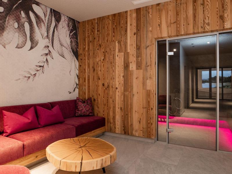 Moderní hotelová lounge s dřevěným obložením, červenou pohovkou a kulatým dřevěným stolem.