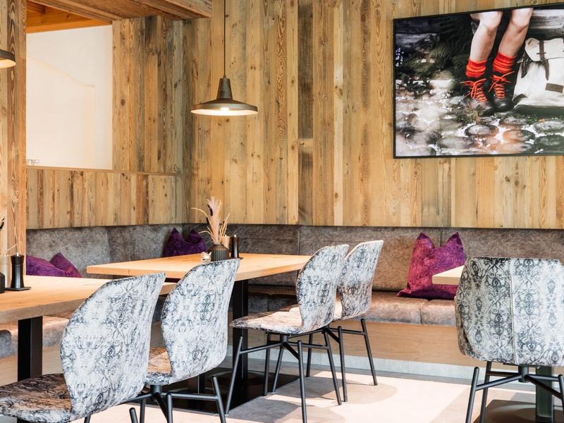 Uklidněná jídelní část s dřevěnými stěnami, polstrovanými lavicemi a moderními židlemi.