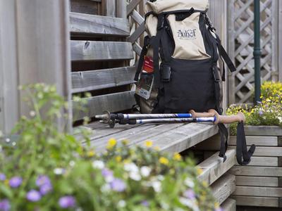 Sac à dos et bâtons de randonnée reposent sur un banc en bois à côté d'une clôture en bois dans un jardin.
