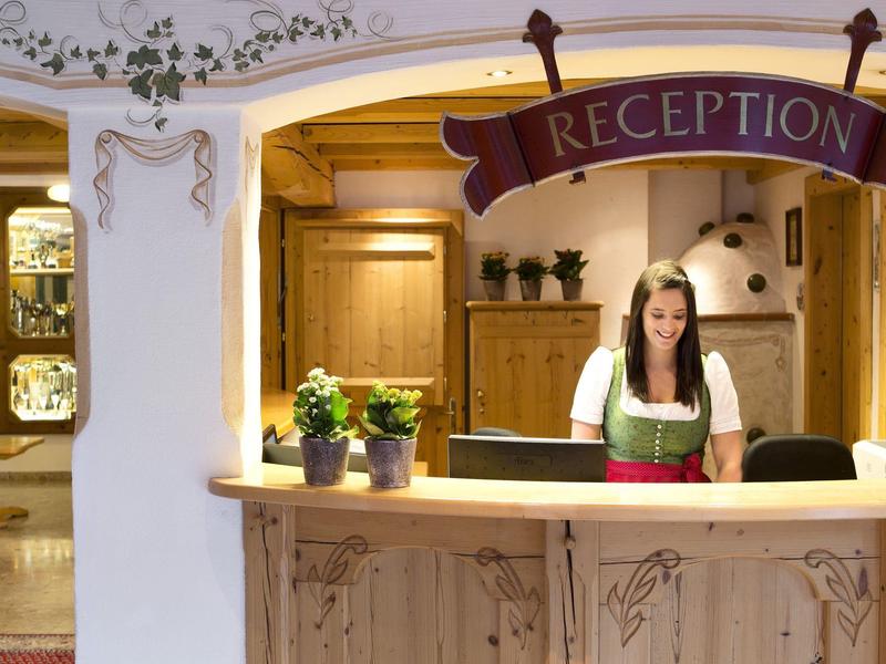 Femme en tenue traditionnelle au comptoir en bois de la réception dans un hôtel chaleureux avec des plantes.