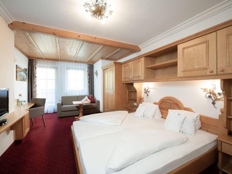 Chambre d'hôtel confortable avec lit double, canapé, TV et grandes fenêtres avec rideaux.