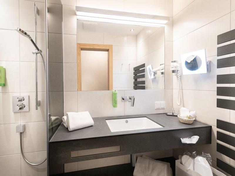Salle de bain moderne avec lavabo, miroir, serviettes et douche dans la chambre d'hôtel.