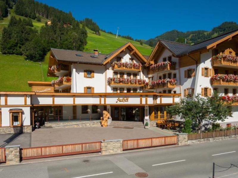 Grand hôtel chalet dans les Alpes avec plusieurs balcons et collines vertes en arrière-plan