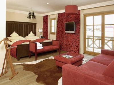 Pohodlný hotelový pokoj s červenou pohovkou, manželskou postelí a světlou dřevěnou podlahou.