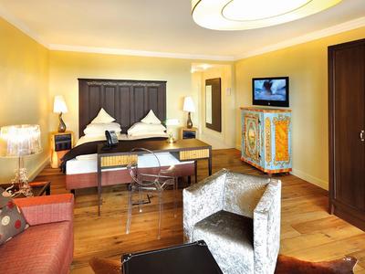 Moderně zařízený hotelový pokoj s manželskou postelí, posezením a televizí.