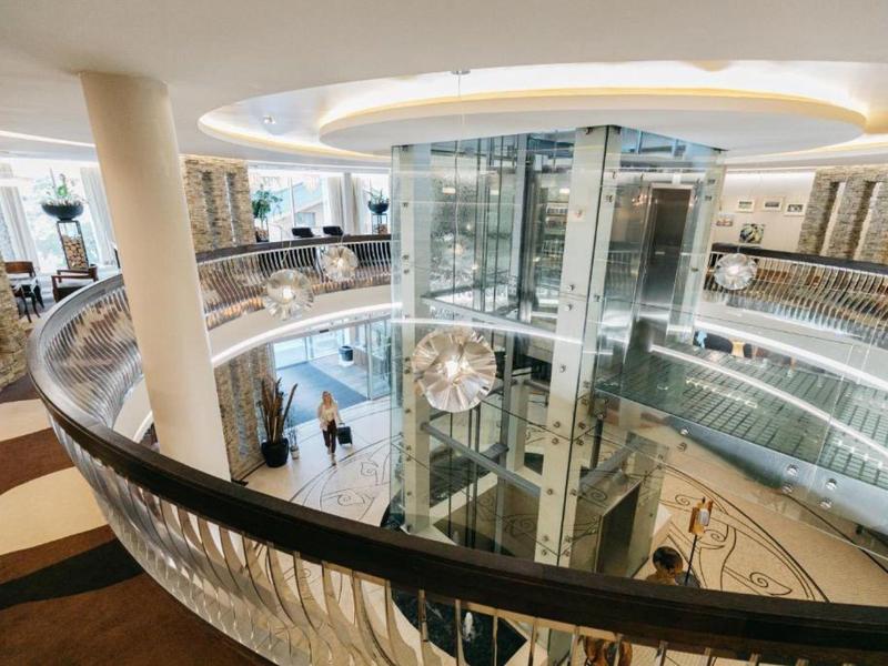 Moderní hotelový interiér se skleněným výtahem a kruhovými schodišti v jasném designu.