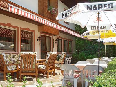 Slunná kavárenská terasa s dřevěnými stoly, židlemi a několika slunečníky.