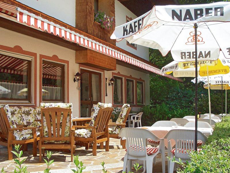 Pohodlné venkovní posezení s slunečníky před hotelem s květinami a zeleným živým plotem.