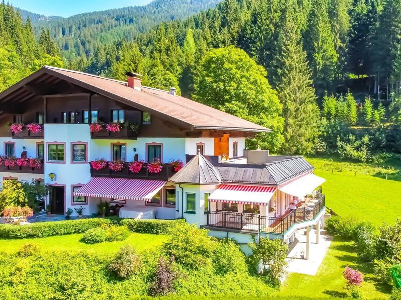 Tradiční chata uprostřed zelených luk a zalesněných hor za slunečného dne.