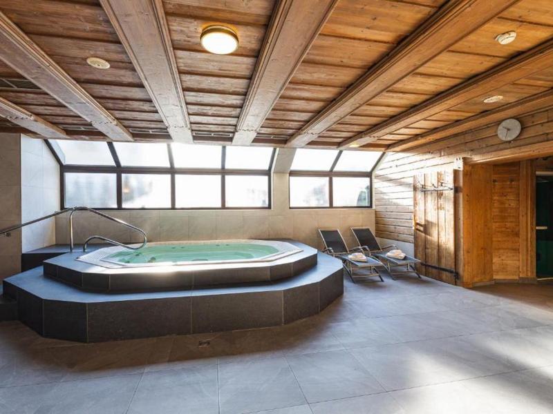 Moderne wellnessruimte met whirlpool, houten plafond, twee ligstoelen en aangrenzende sauna.