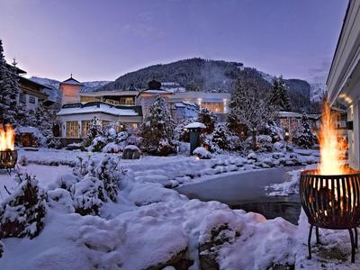 Snow-covered hotel grounds with burning fire bowls and mountain in the background at dusk.