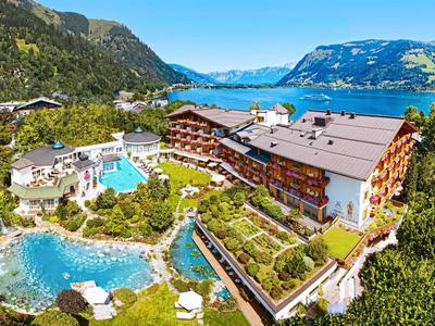 Hotel complex with outdoor pool, pond, and mountain views in a green landscape.