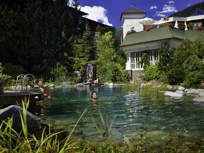 A hotel with a natural swimming pond surrounded by greenery under a blue sky.