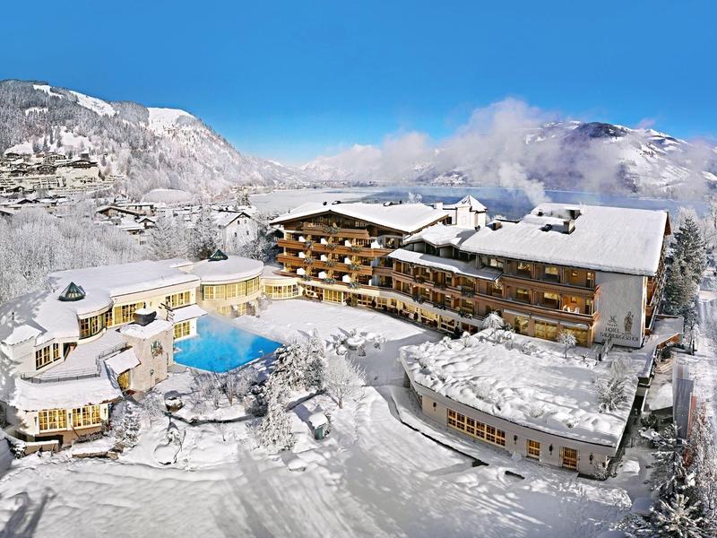 Large hotel with outdoor pool in snowy mountain landscape under clear sky.