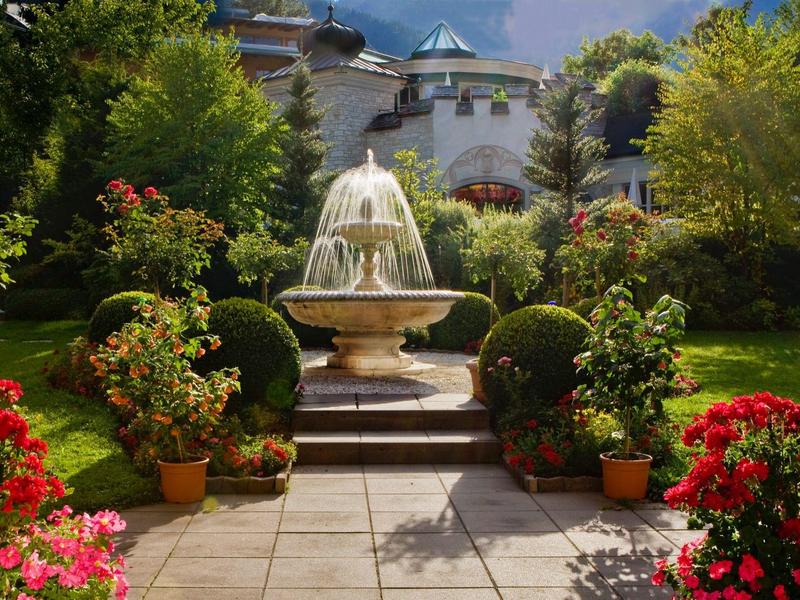 Decorative fountain in a blooming garden in front of an elegant hotel building.