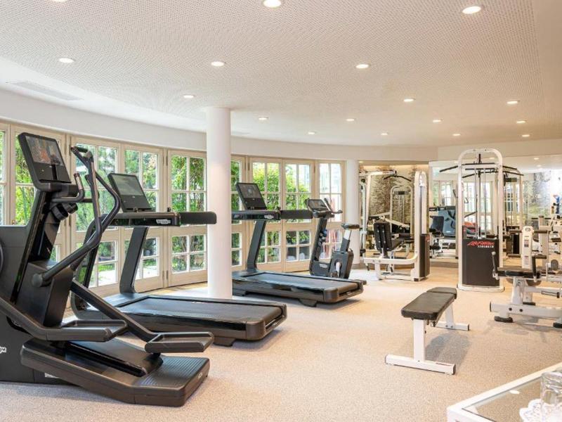 Bright gym with treadmills, bikes, and strength equipment featuring large windows.