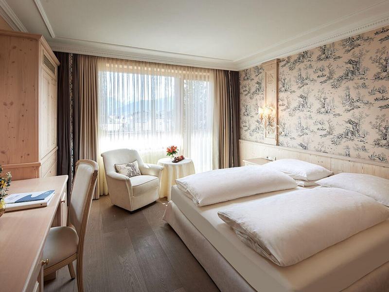 Cozy hotel room with double bed, armchair, desk, and large window with curtains.