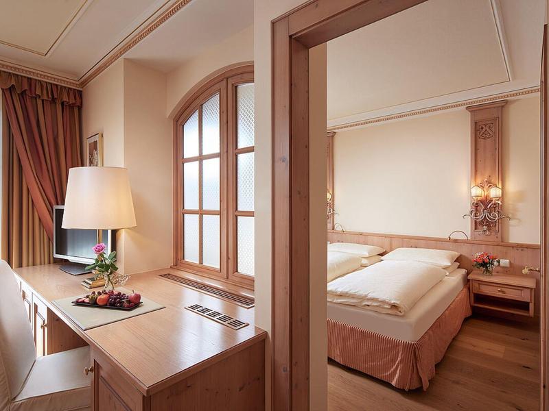 Bright hotel room with desk, chair, and double bed in warm tones.