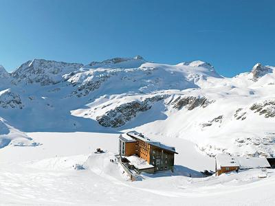 Einsames Chalet in verschneiter Berglandschaft unter klarem blauem Himmel.