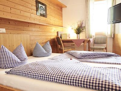 Helles Schlafzimmer mit Holzverkleidung, karierten Bettdecken, Tisch, Stühlen und Fenster mit Gardinen.