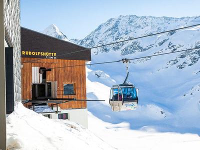 Bergbahn-Gondel vor verschneitem Bergpanorama neben Holzhütte